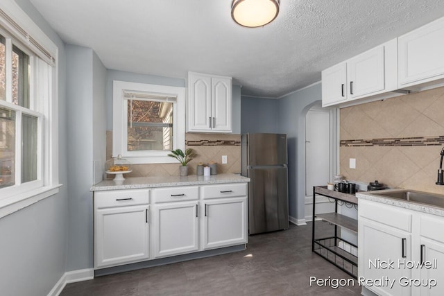 kitchen with baseboards, arched walkways, freestanding refrigerator, a sink, and white cabinetry