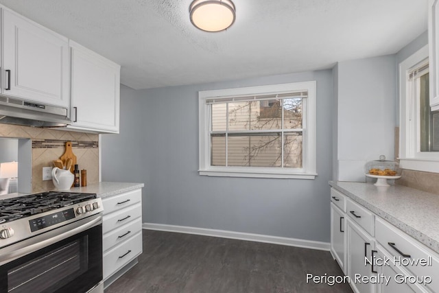 kitchen featuring stainless steel gas range oven, under cabinet range hood, dark wood finished floors, decorative backsplash, and baseboards