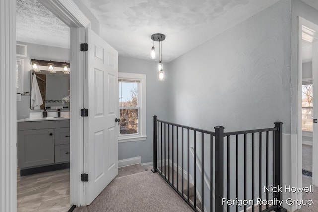 hall with an upstairs landing, visible vents, light colored carpet, and a textured ceiling