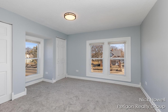 carpeted empty room featuring baseboards, plenty of natural light, and a textured ceiling