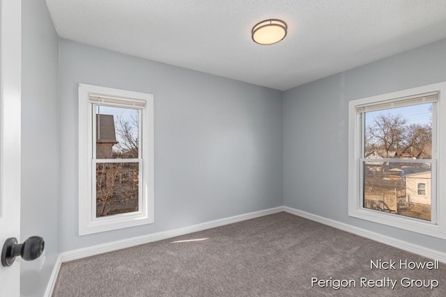 carpeted spare room featuring a healthy amount of sunlight and baseboards