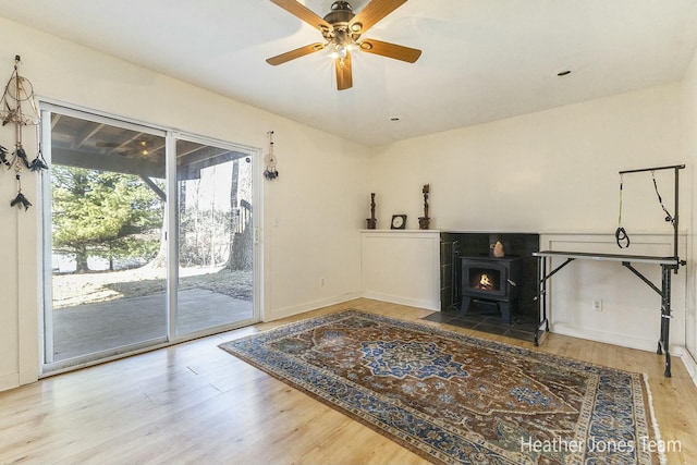 living room with ceiling fan, baseboards, wood finished floors, and a wood stove