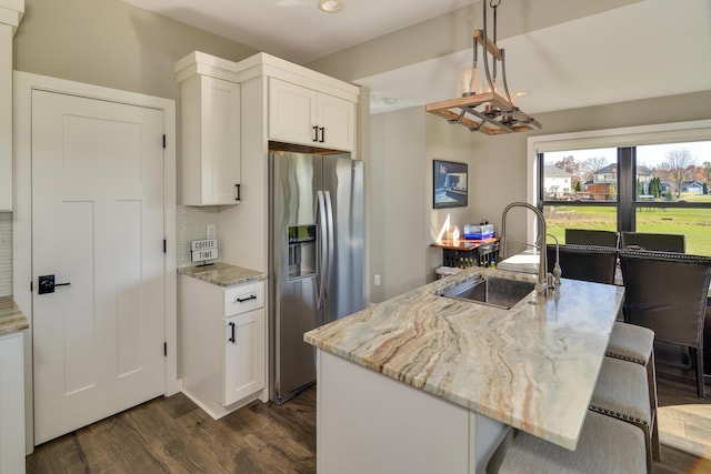 kitchen featuring a sink, backsplash, light stone countertops, stainless steel fridge, and dark wood-style flooring