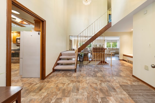 staircase featuring visible vents, baseboards, a high ceiling, and stone finish floor