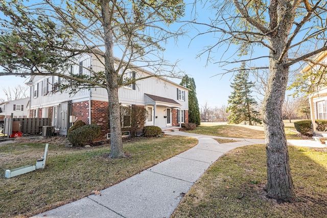 view of front facade featuring brick siding, central AC unit, a front yard, and fence