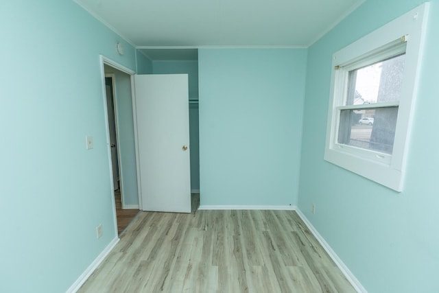 unfurnished bedroom featuring a closet, wood finished floors, baseboards, and ornamental molding