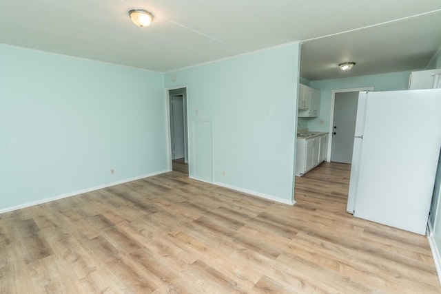 empty room featuring a sink, light wood-style floors, baseboards, and ornamental molding