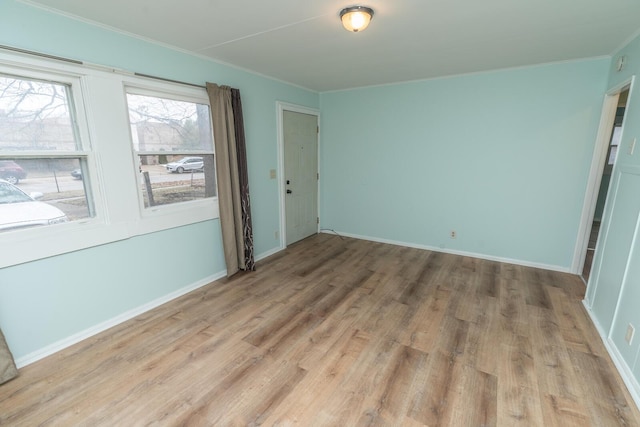 empty room featuring baseboards, light wood-style flooring, and crown molding