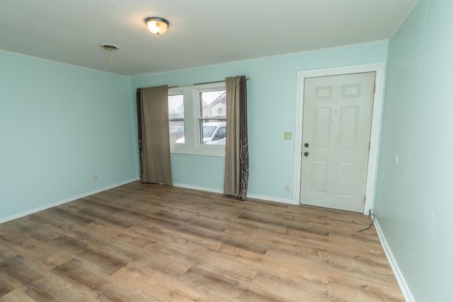 empty room featuring visible vents, baseboards, light wood-style flooring, and ornamental molding