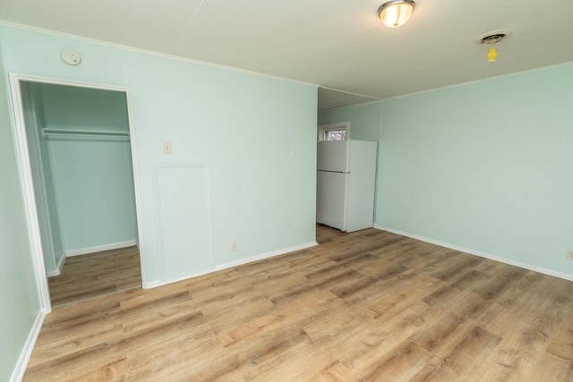 unfurnished bedroom featuring wood finished floors, visible vents, freestanding refrigerator, and ornamental molding