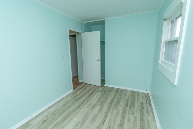 unfurnished bedroom with a closet, crown molding, baseboards, and wood finished floors