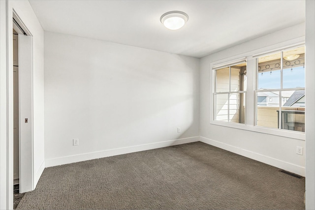 unfurnished room with visible vents, dark carpet, and baseboards