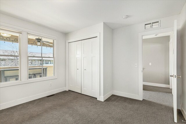 unfurnished bedroom with dark colored carpet, visible vents, baseboards, and a closet