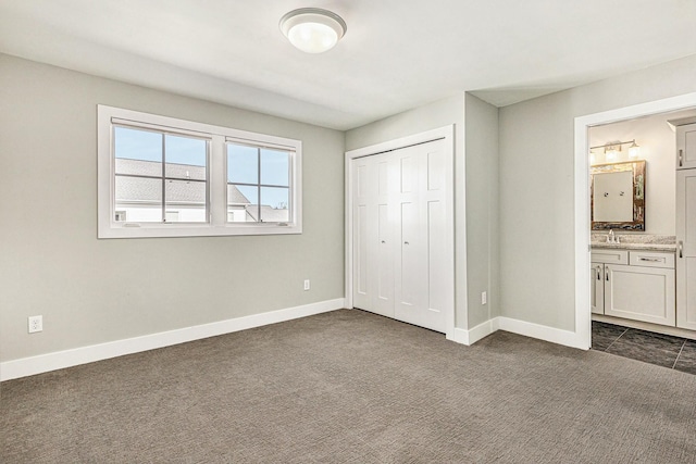 unfurnished bedroom with baseboards, ensuite bath, a sink, a closet, and dark carpet