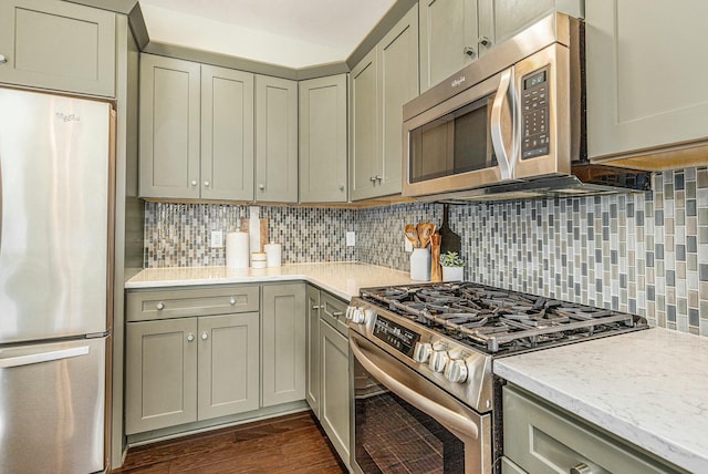 kitchen with tasteful backsplash, light stone countertops, dark wood finished floors, gray cabinets, and appliances with stainless steel finishes