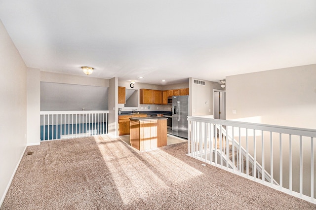 kitchen with brown cabinetry, baseboards, a kitchen island, stainless steel fridge with ice dispenser, and light colored carpet