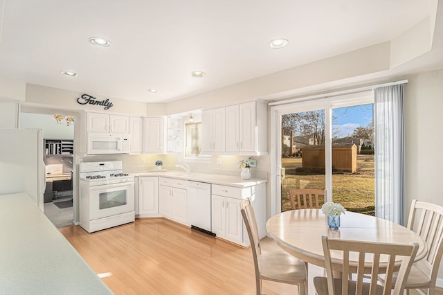 kitchen with a sink, white appliances, light wood-style floors, white cabinets, and light countertops