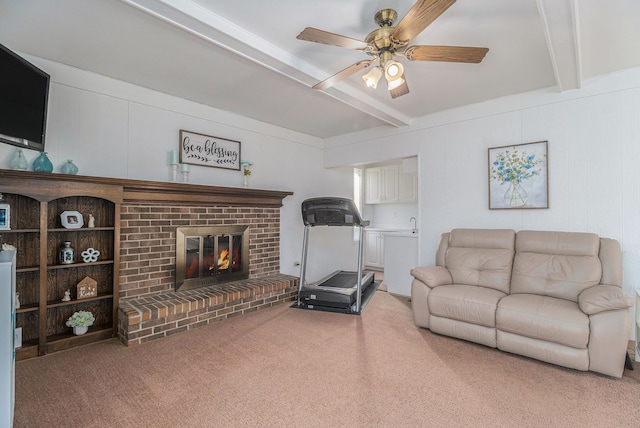 living room featuring beam ceiling, light colored carpet, a brick fireplace, and ceiling fan