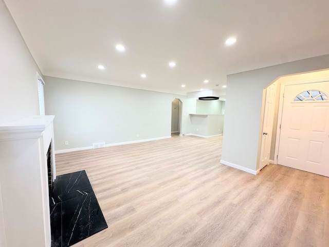 unfurnished living room featuring visible vents, light wood-style flooring, recessed lighting, arched walkways, and baseboards