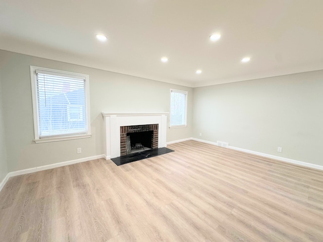 unfurnished living room featuring visible vents, baseboards, recessed lighting, light wood-style floors, and a brick fireplace
