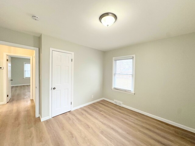 unfurnished bedroom with multiple windows, visible vents, light wood-type flooring, and baseboards