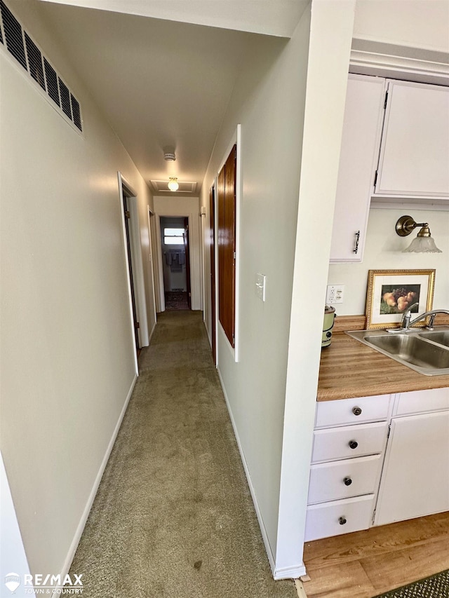 hall featuring baseboards, visible vents, carpet floors, and a sink