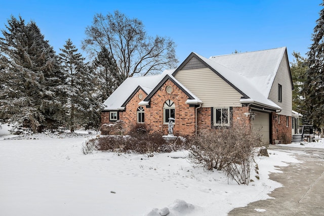 view of snow covered exterior featuring brick siding and a garage