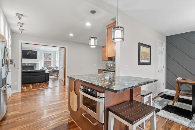 kitchen with a kitchen bar, a high end fireplace, light wood-style floors, appliances with stainless steel finishes, and decorative backsplash