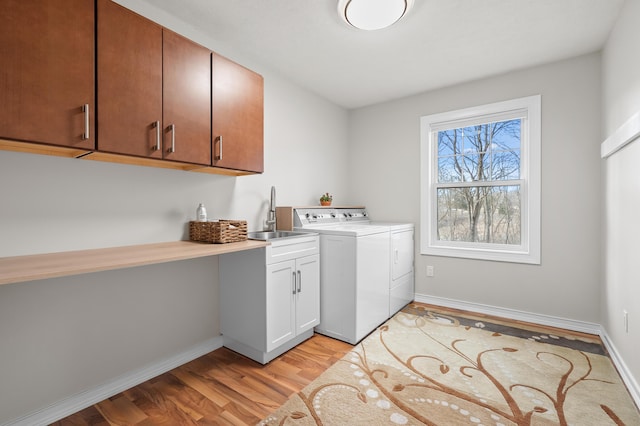 laundry room featuring light wood-style flooring, a sink, washer and dryer, cabinet space, and baseboards