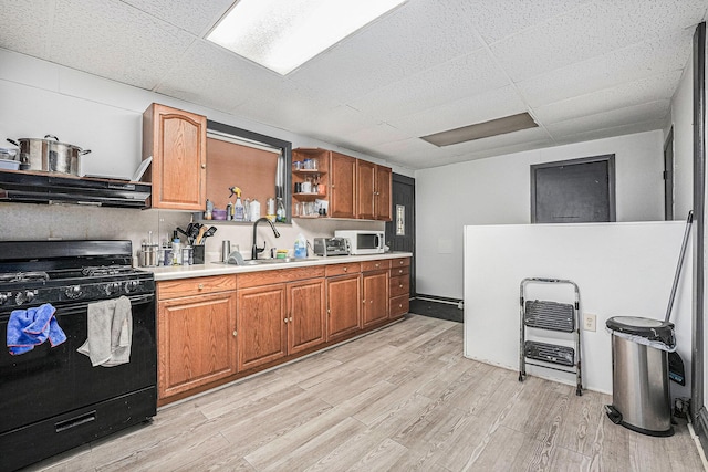 kitchen featuring range hood, open shelves, a sink, light wood-style floors, and black range with gas cooktop