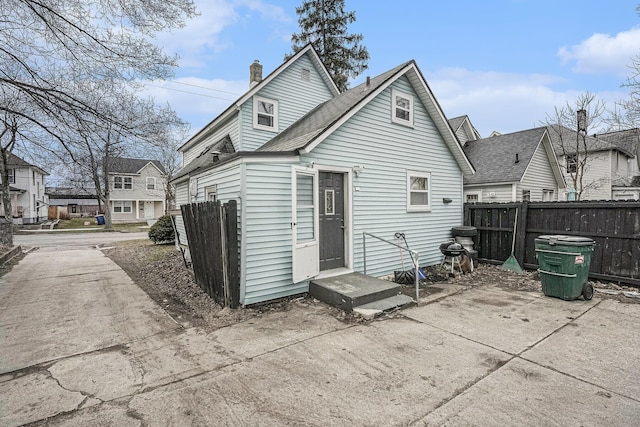 rear view of house featuring entry steps, fence, and a chimney