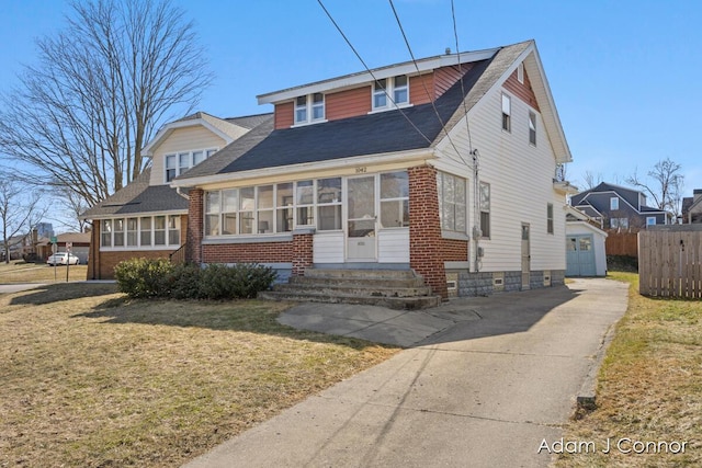 view of front of home with brick siding, entry steps, a front yard, an outdoor structure, and a sunroom