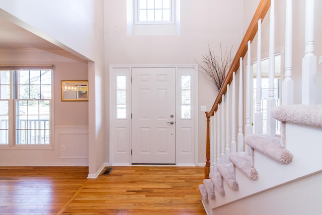 entrance foyer with stairway, light wood-style floors, a wealth of natural light, and wainscoting