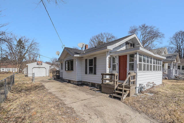 bungalow featuring fence, concrete driveway, a garage, a sunroom, and an outbuilding