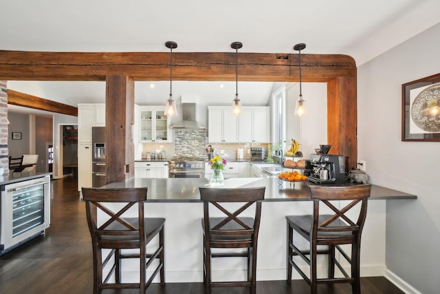 kitchen with beverage cooler, a peninsula, stainless steel appliances, wall chimney range hood, and backsplash