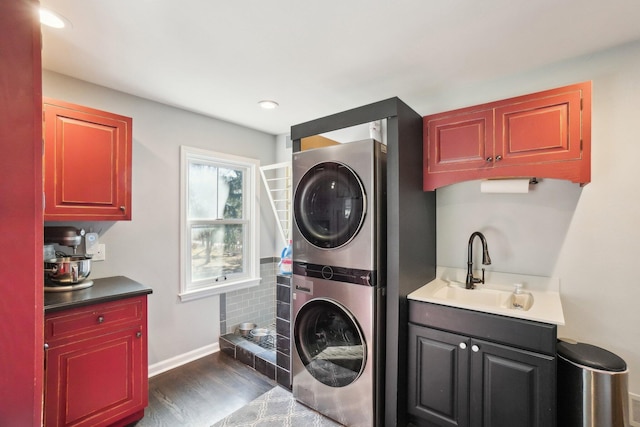 washroom with baseboards, dark wood finished floors, laundry area, stacked washer / drying machine, and a sink