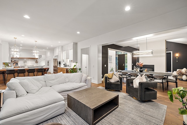 living room featuring a glass covered fireplace, recessed lighting, light wood-type flooring, and a chandelier