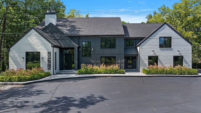 view of front facade featuring brick siding, roof with shingles, and a chimney