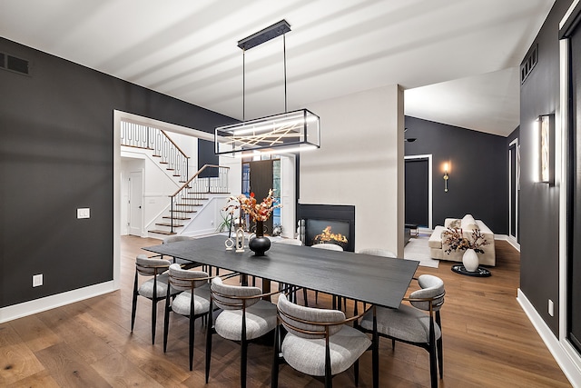 dining space with visible vents, baseboards, stairway, a warm lit fireplace, and wood finished floors