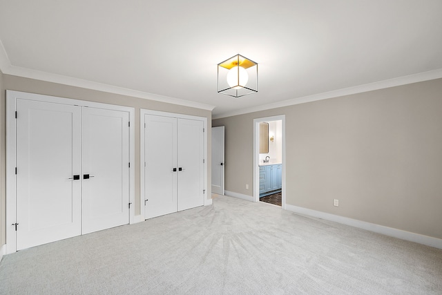 unfurnished bedroom featuring connected bathroom, two closets, baseboards, ornamental molding, and carpet floors