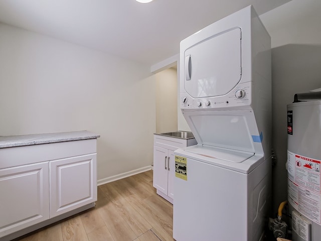 clothes washing area with baseboards, cabinet space, water heater, light wood-style floors, and stacked washer / drying machine