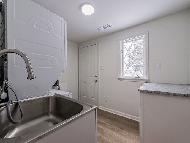 clothes washing area with baseboards, visible vents, light wood finished floors, stacked washing maching and dryer, and a sink