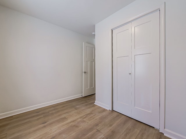 unfurnished bedroom featuring light wood-type flooring, baseboards, and a closet