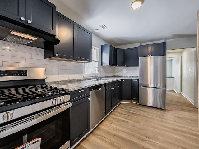 kitchen featuring under cabinet range hood, light stone counters, light wood-style flooring, appliances with stainless steel finishes, and a sink