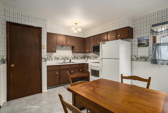 kitchen with wallpapered walls, light countertops, a notable chandelier, white appliances, and a sink