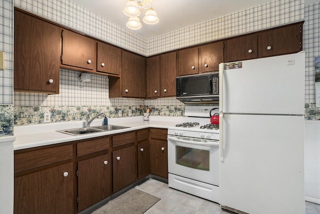 kitchen with wallpapered walls, white appliances, light countertops, and a sink