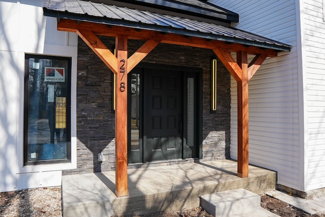 doorway to property with stone siding, a porch, and metal roof