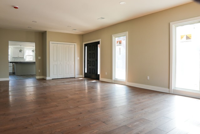 unfurnished living room with dark wood-style floors, baseboards, and a wealth of natural light