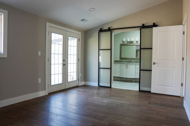 interior space with a barn door, a healthy amount of sunlight, vaulted ceiling, and french doors