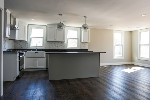 kitchen with dark wood-type flooring, a sink, dark countertops, wall chimney exhaust hood, and stainless steel range with gas stovetop